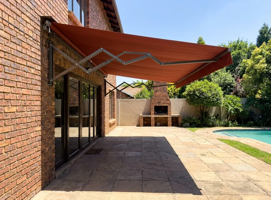 A rust-red folding-arm awning bolted above the patio doors of a Hurlingham home and opened right out over the paving, braai and pool alongside